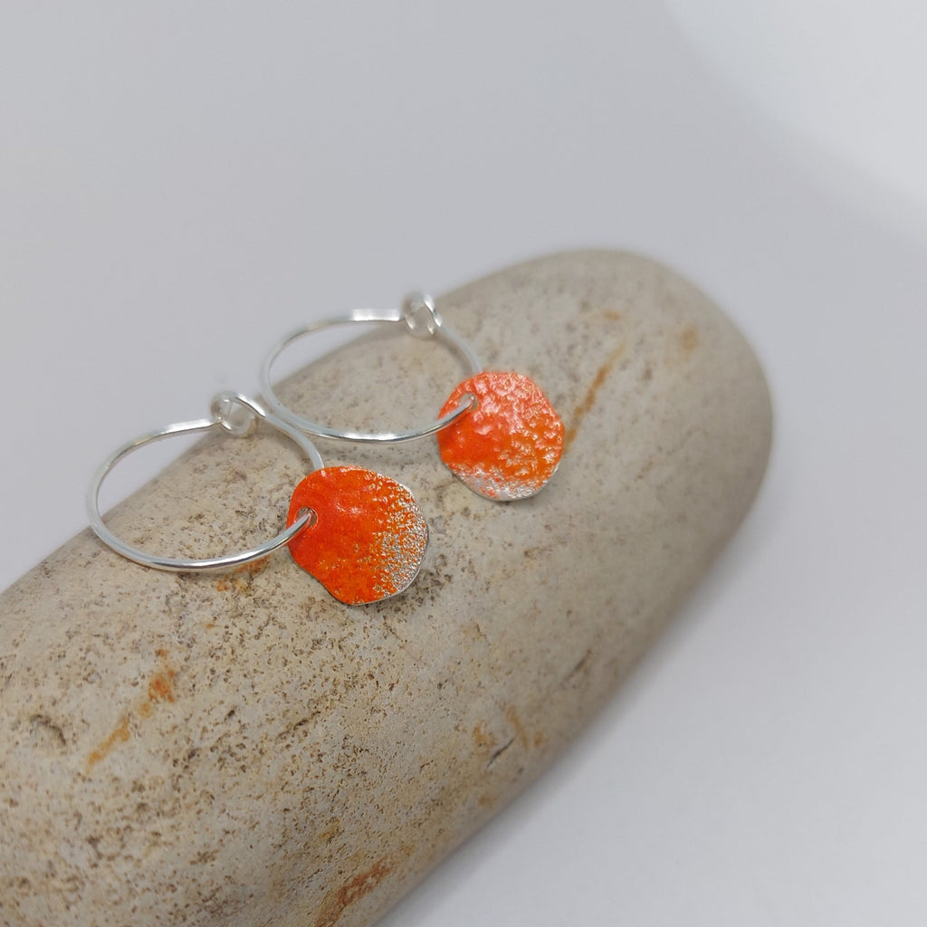 Sterling silver hoop earrings with a sterling silver organic shape hanging from the hoop which has been powder coated in bright orange. Bay of fires , Tasmania.