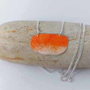 Organic shape sterling silver necklace with orange powder coat detail on a rock.