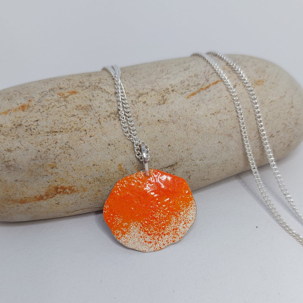 Sterling silver organic shape necklace with orange powder coat on a rock.