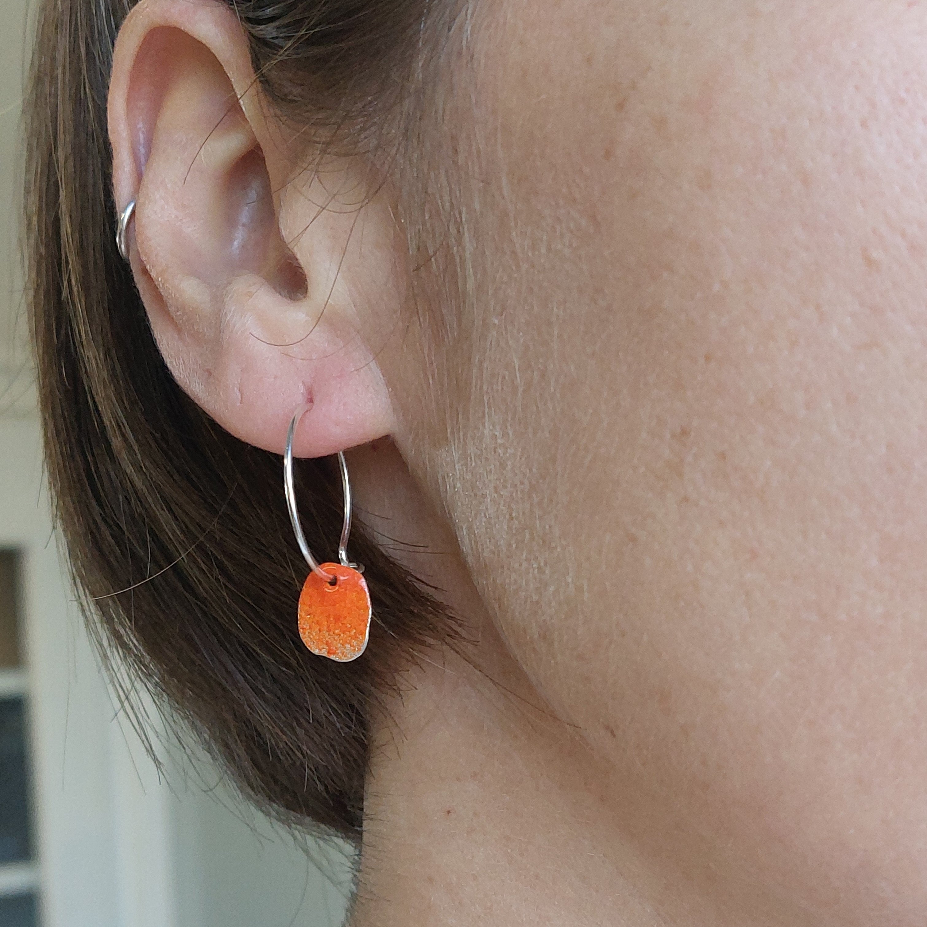 Sterling silver hoop earrings with a sterling silver organic shape hanging from the hoop which has been powder coated in bright orange. Bay of fires , Tasmania.