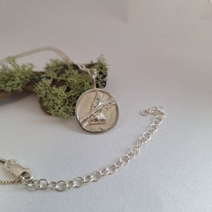 Sterling silver forest inspired necklace with branch shape resting on a lichen covered branch