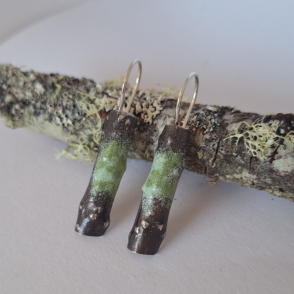 Sterling silver powder coated lichen inspired earrings resting on a lichen covered branch