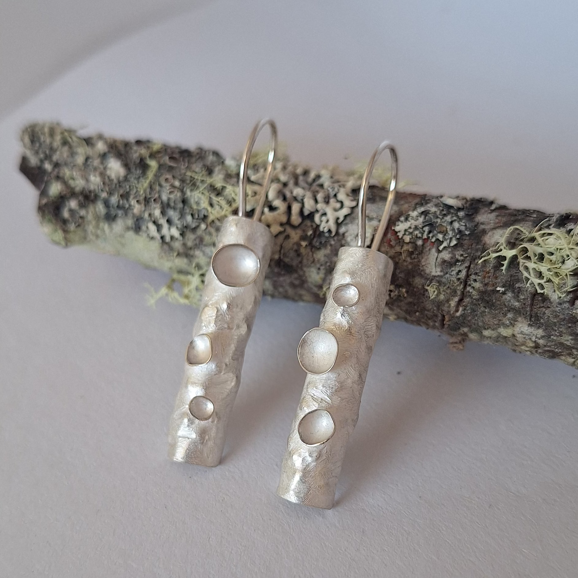 Sterling silver lichen inspired earrings resting on a lichen covered branch